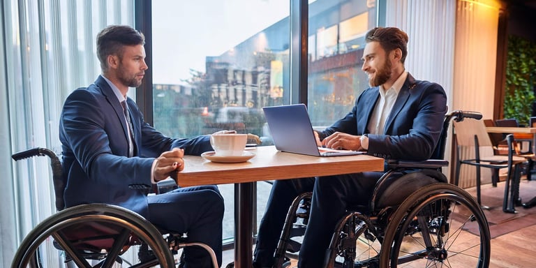 Zwei Rollstuhlfahrer sitzen für ein Beratungsgespräch in einem Café
