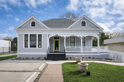 Restored light gray Victorian cottage with a white porch railing and yellow front door.