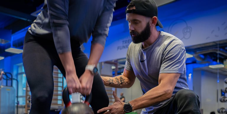 Trener instruuje kobietę przy treningu z kettlebell.
