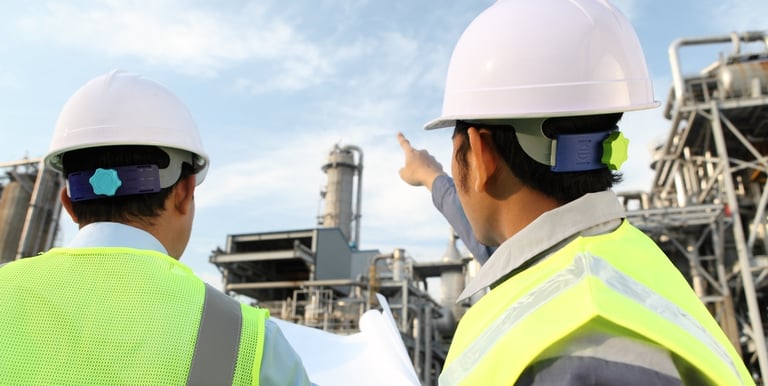 two men in safety vests standing in front of a factory
