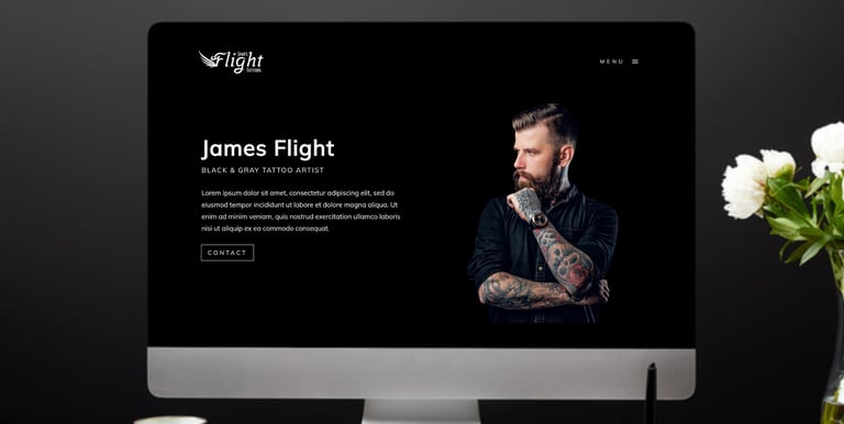 a computer screen on a desk featuring the homepage of a tattoo artist website