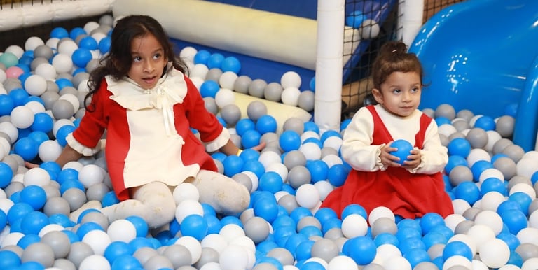 two young girls in red and white dresses playing in a ball pit in gurugram trumpy softplay