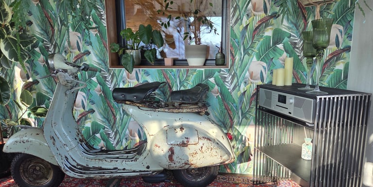 Vintage-Vespa als dekoratives Highlight vor Dschungel-Tapete neben modernem Holz-Sideboard.