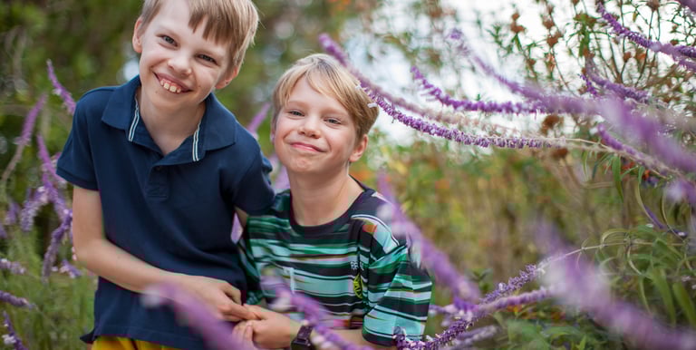 Two brothers share a happy moment surrounded by purple wildflowers in Pestana Grand, Madeira, natural lifestyle family photo.