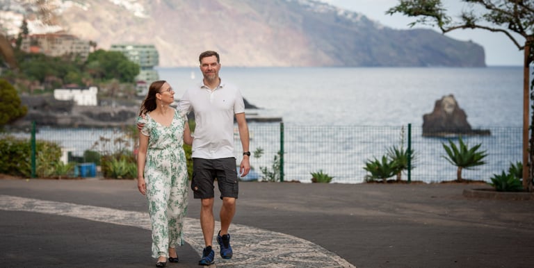 Couple walks along Funchal Lido Promenade, Madeira, with Atlantic coast and scenic cliffs in the background, lifestyle mood.