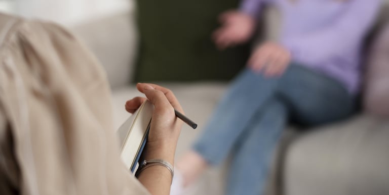 Eine Frau sitzt auf der Couch und eine andere Frau sitzt ihr gegenüber, mit einem Stift in der Hand