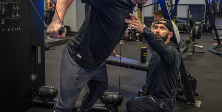 Trener instruuje podopiecznego gdy ten wykonuje ćwiczenie na siłowni.