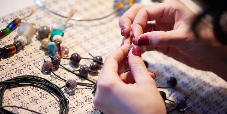Manos de artista ensamblando un collar de cuentas hecho a mano usando cuentas de vidrio y cordón.