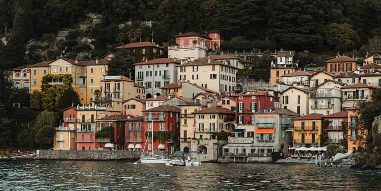 a bunch of houses on a hill with a boat in the water varenna lake como