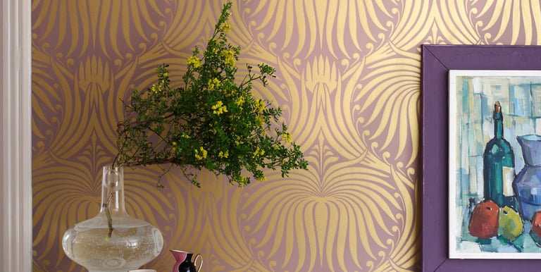 Elegant gold art deco wallpaper pattern behind a marble counter with a glass vase and framed art.