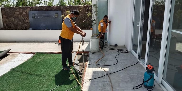 Professional pest control technicians in yellow vests applying termite treatment to a residential patio.