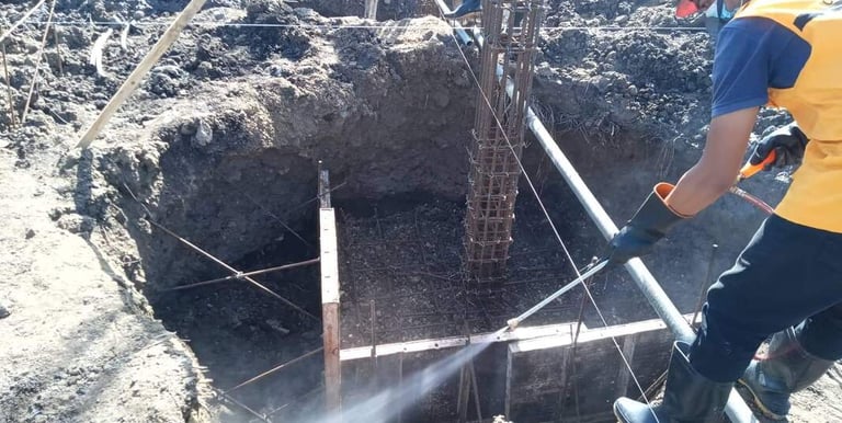A exterminator in safety gear uses a high-pressure water hose for soil compaction at a site.