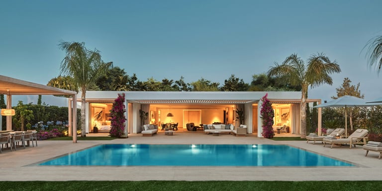 Luxury modern villa at dusk at Ikos Andalucía, blue swimming pool and elegant outdoor patio lounge.