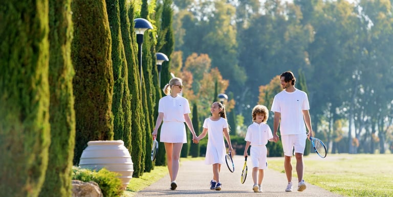 A family wearing white tennis apparel walking together on a sunny path at a luxury resort.