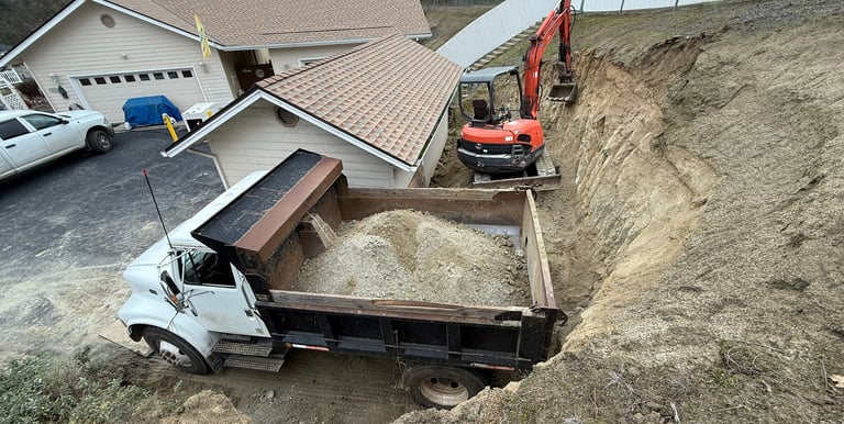Excavator digging around building, dump truck full of dirt in front