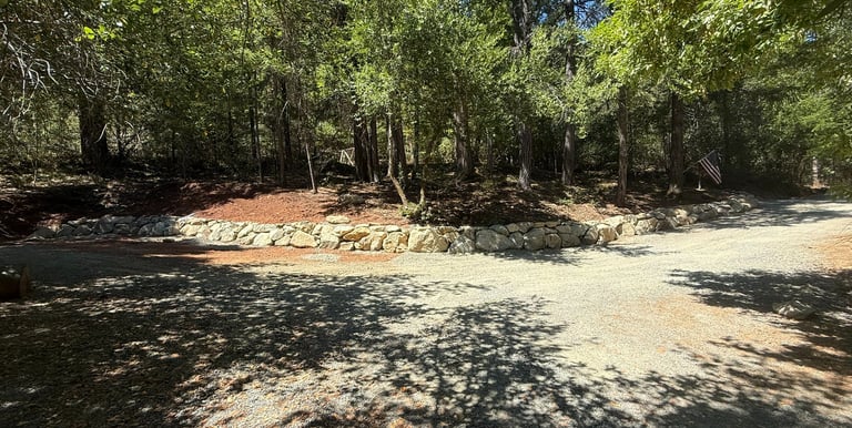 Rock wall with driveway in front and trees behind