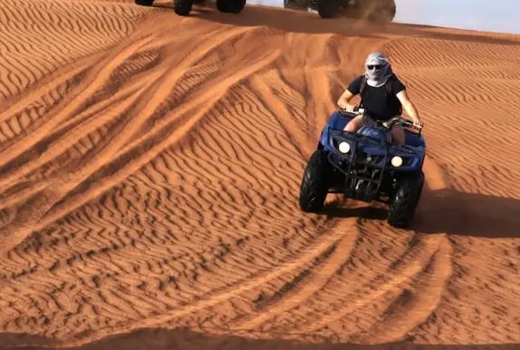 Tourist riding a quad bike on Dubai desert sand dunes during a desert safari