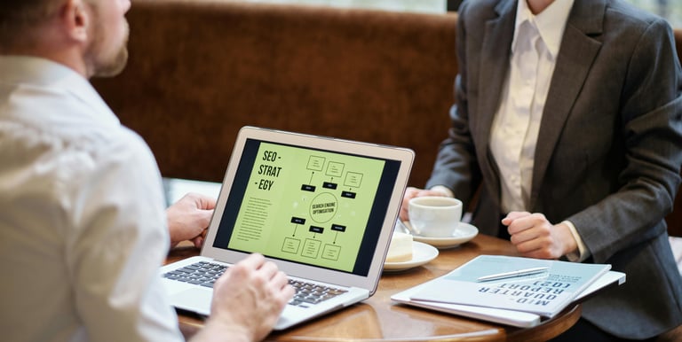 Two business professionals reviewing an SEO strategy flowchart on a laptop in a cafe setting.