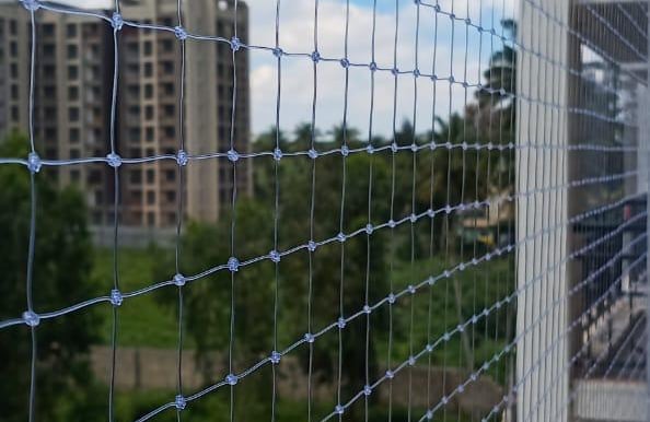 A technician carefully installing a sturdy safety net on a residential balcony in Chennai.