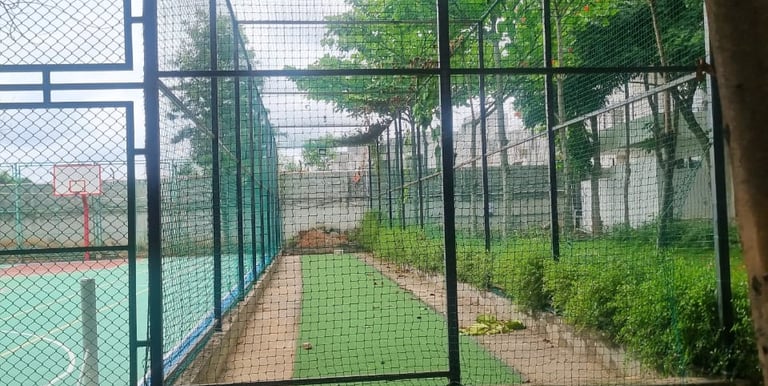A technician carefully installing a cricket net on a sunny Chennai playground.
