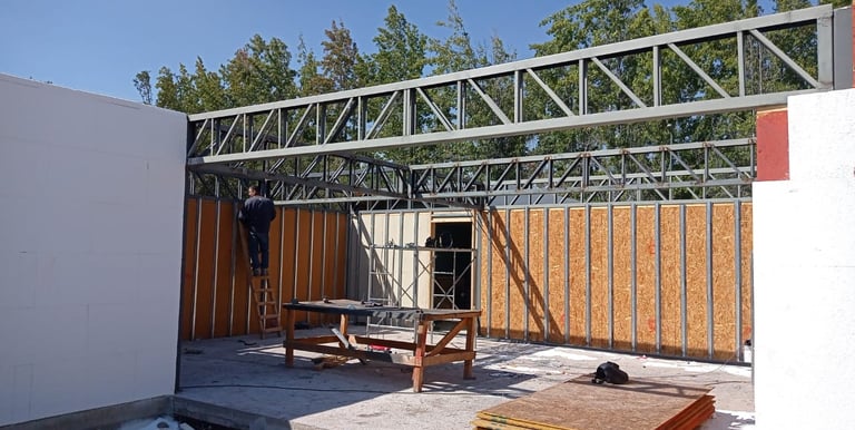 Obra en construcción donde se muestran las cerchas de acero que se están instalando en muros blancos