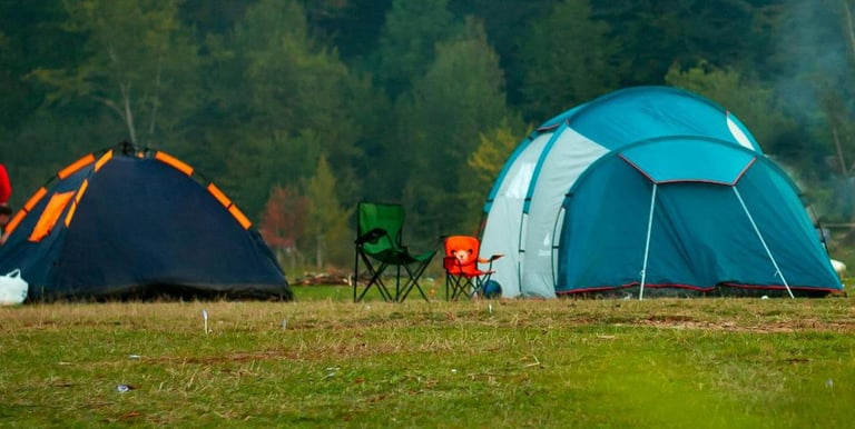 Two camping tents and foldable chairs set up on a grassy field