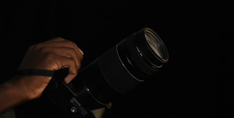 A person's hand holding a professional Canon DSLR camera with a long telephoto lens against a black background.