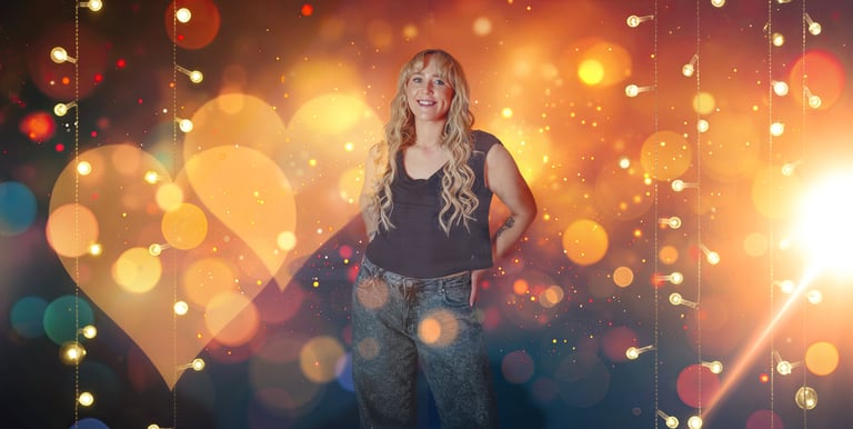Smiling blonde woman posing in front of festive bokeh heart lights and golden holiday glitter.