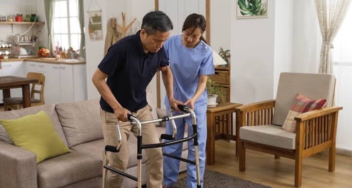 home physiotherapist helping a neurological patient walk using a walker for balance.