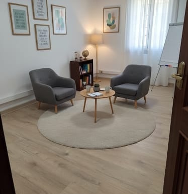 Modern therapy room with two grey armchairs, a round rug, and framed wall art on wood floors.