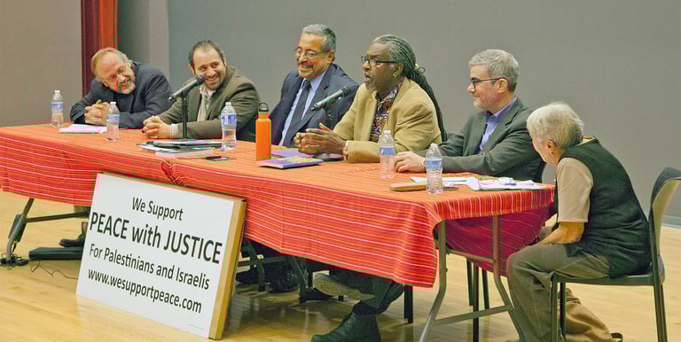 A panel of speakers sit at a table with a sign saying we support peace with justice for palestinians