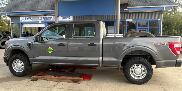 A gray Ford F-150 truck lifted on a red hydraulic jack at an automotive tire and brake service shop.