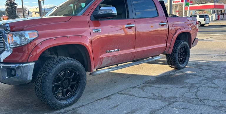 Red Toyota Tundra pickup truck with black off-road wheels parked at a gas station.