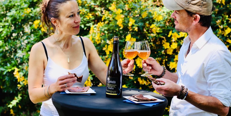 Couple en train de trinquer avec du cidre et qui déguste des galettes sur une table à l'extérieur