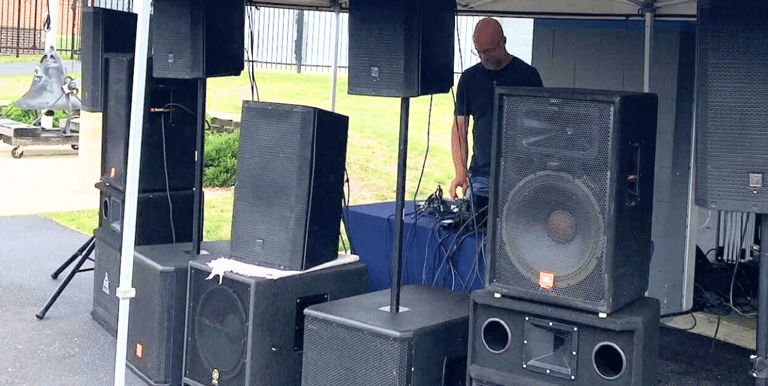 man outdoors under a tent standing behind speakers