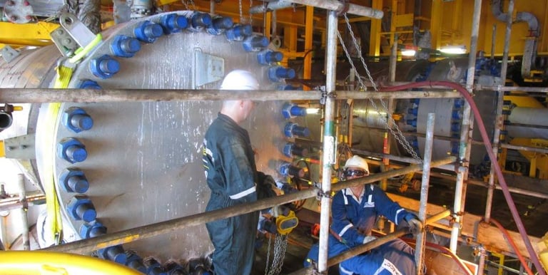 Industrial technicians performing maintenance on a large heat exchanger at an offshore oil rig.