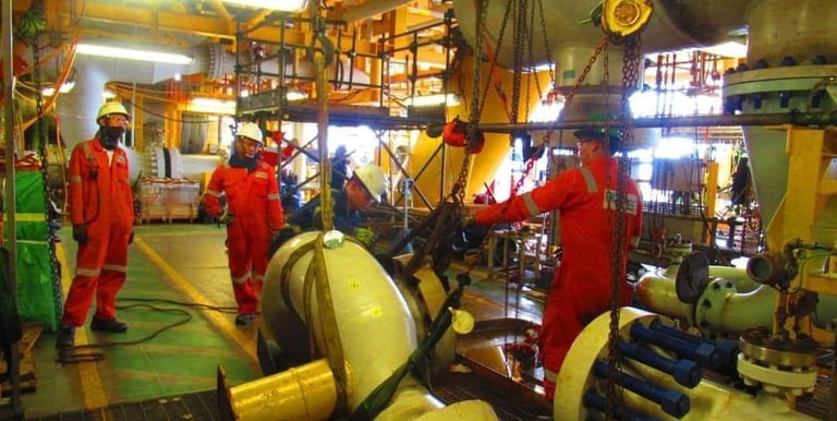 Offshore oil rig engineers in orange coveralls performing heavy lifting and pipeline maintenance.
