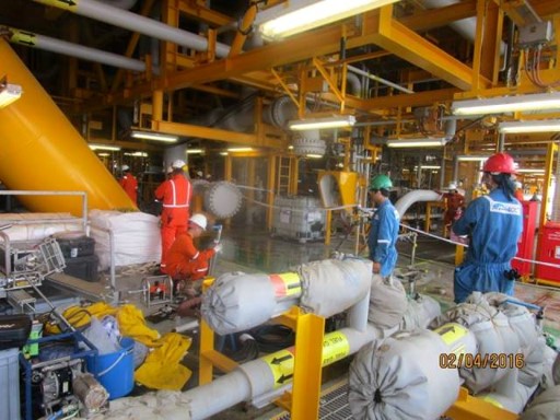 Industrial offshore oil rig workers wearing safety gear performing maintenance on yellow steel pipes.