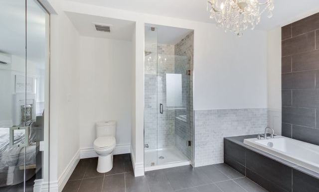 a large master bathroom with a toilet, shower stall, and soaker tub tiled in black