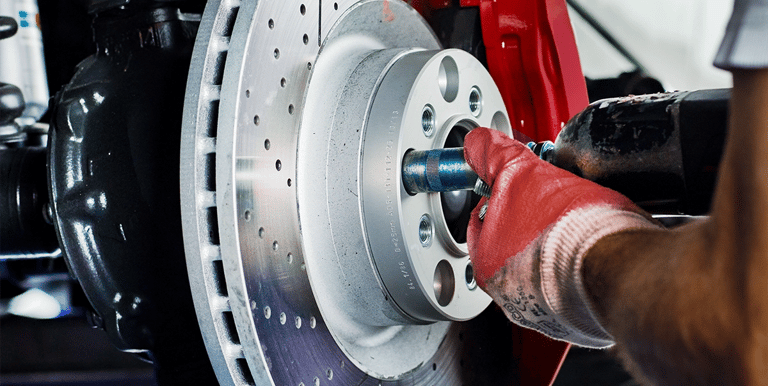 person with red gloves holding a car tool fixing a brake.