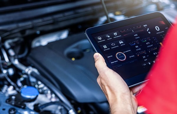 man holding a tablet analyzing a car's engine.