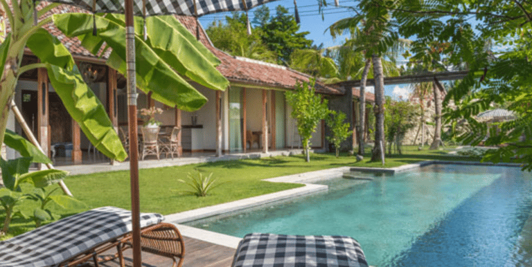 Shimmering swimming pool surrounded by tropical plants, sun loungers, and joglo with modern amenity