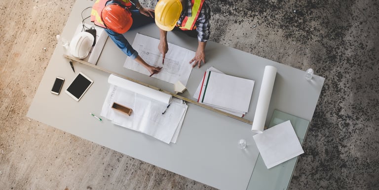two men in safety vests and hard hats working on a table