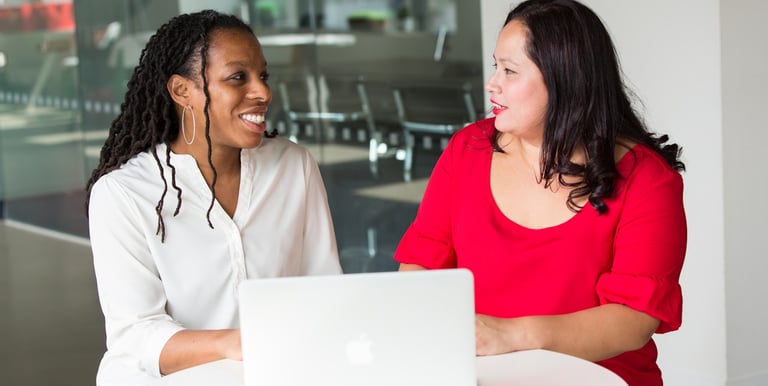two women sitting at a table with a laptop