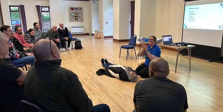 a group of people sitting in chairs in a room watching a first aid training demonstration