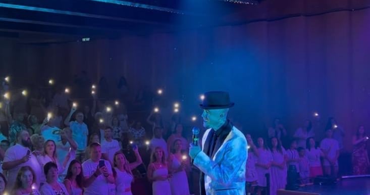 a man in a white shirt and a microphone in front of a crowd