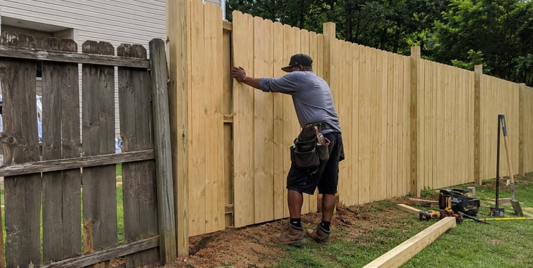 A professional contractor installing a new cedar wood privacy fence in a residential backyard.