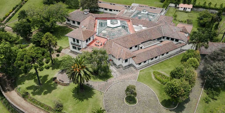 Fotografía con dron de mansión colonial de paredes blancas con techo naranja, cúpulas rodeada de naturaleza Quito Ecuador