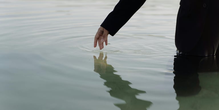 “Silhouet van persoon staand in water, hand raakt oppervlak, symboliseert introspectie.