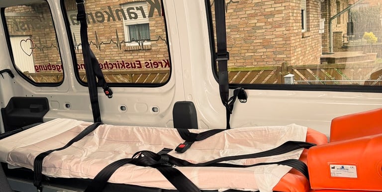 Innenraum eines Krankenfahrdienstes mit leerer Trage neben Fenster Backsteingebäude außen sichtbar.